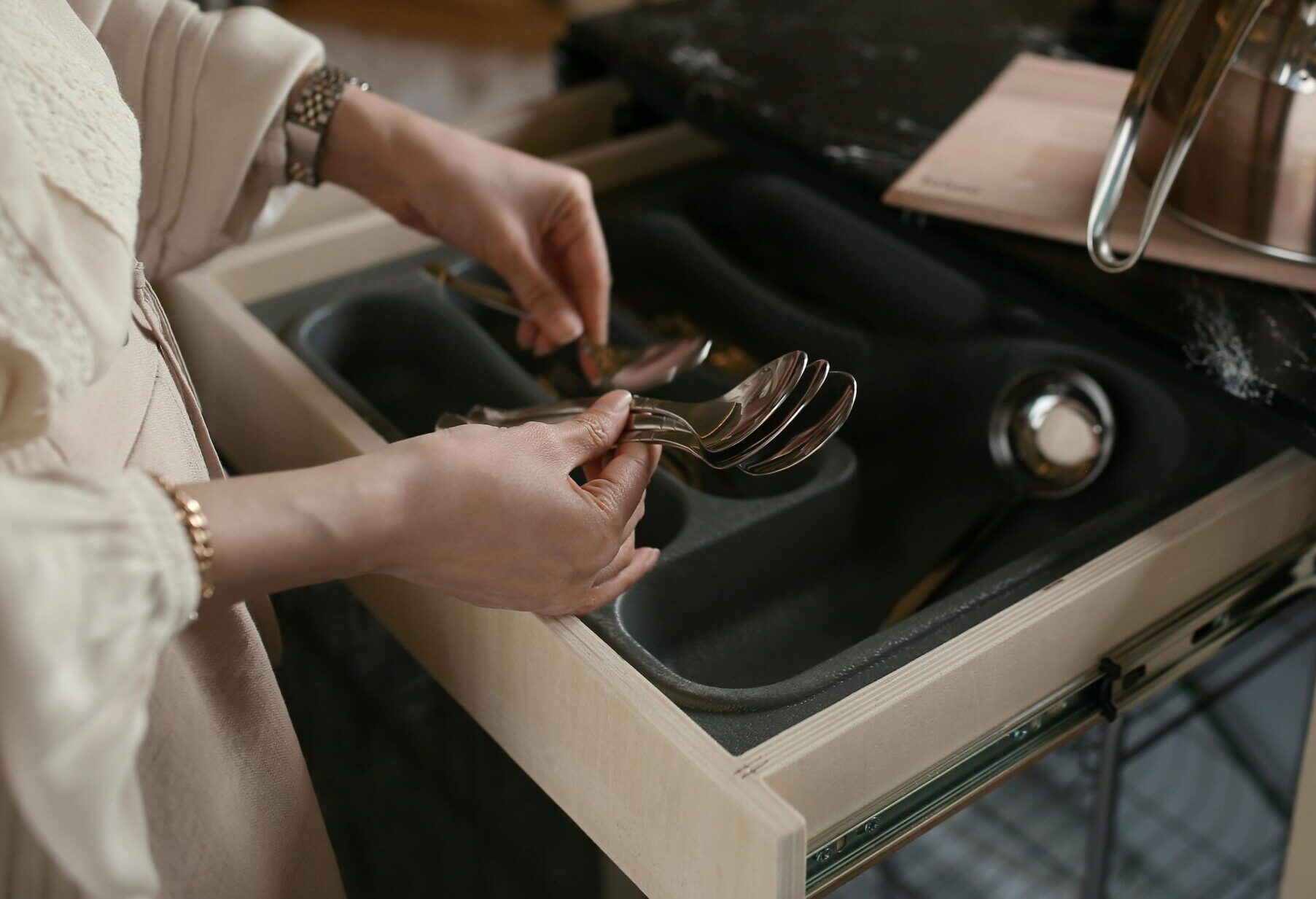 pexels photo 12329332 12329332 A woman organizing spoons in a kitchen drawer beside a stainless steel kettle.