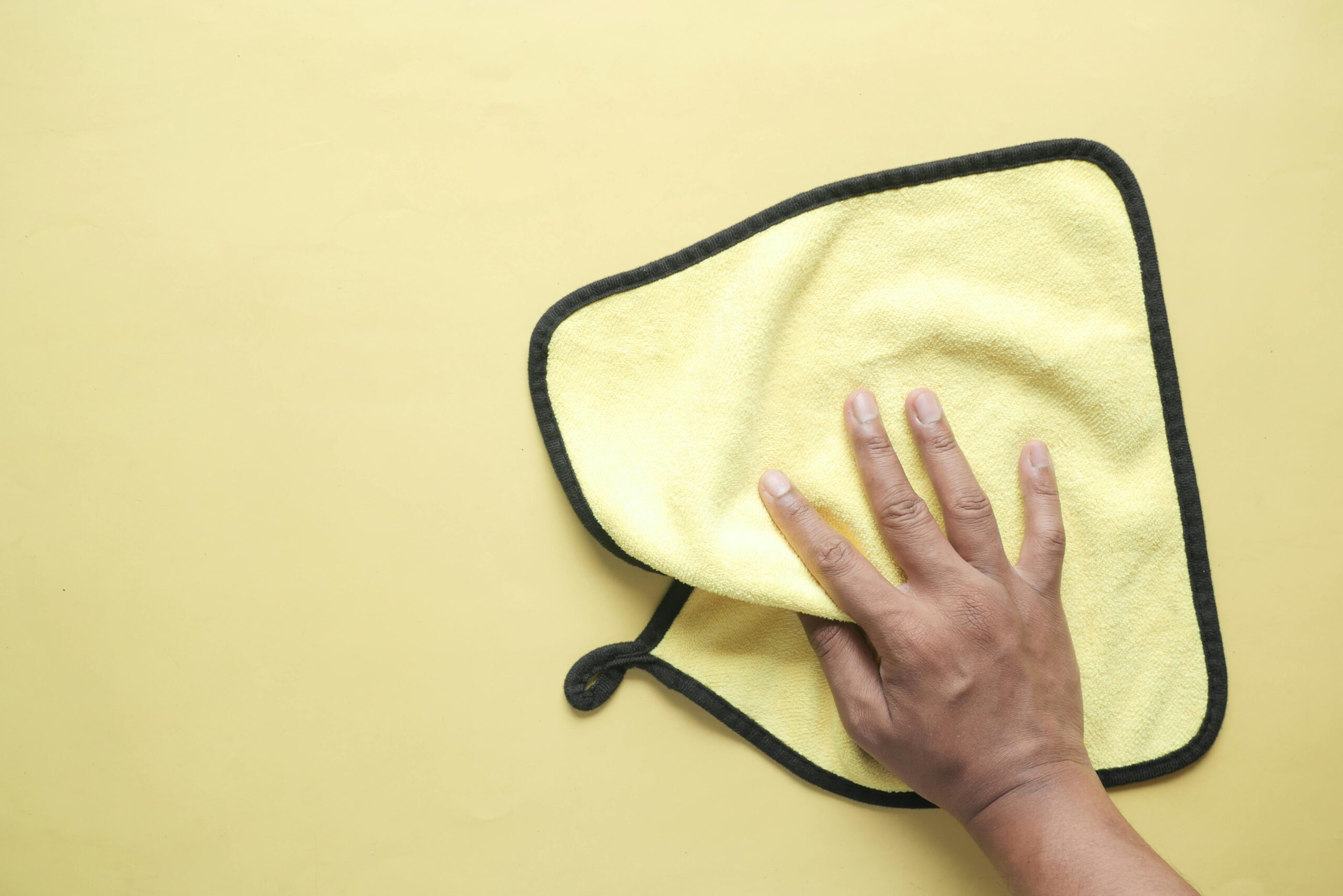 pexels photo 12349434 12349434 A hand using a microfiber cloth to wipe a yellow background, demonstrating cleaning and hygiene concepts.