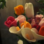 About A vibrant bouquet of crocheted flowers in various colors, arranged in a vase.