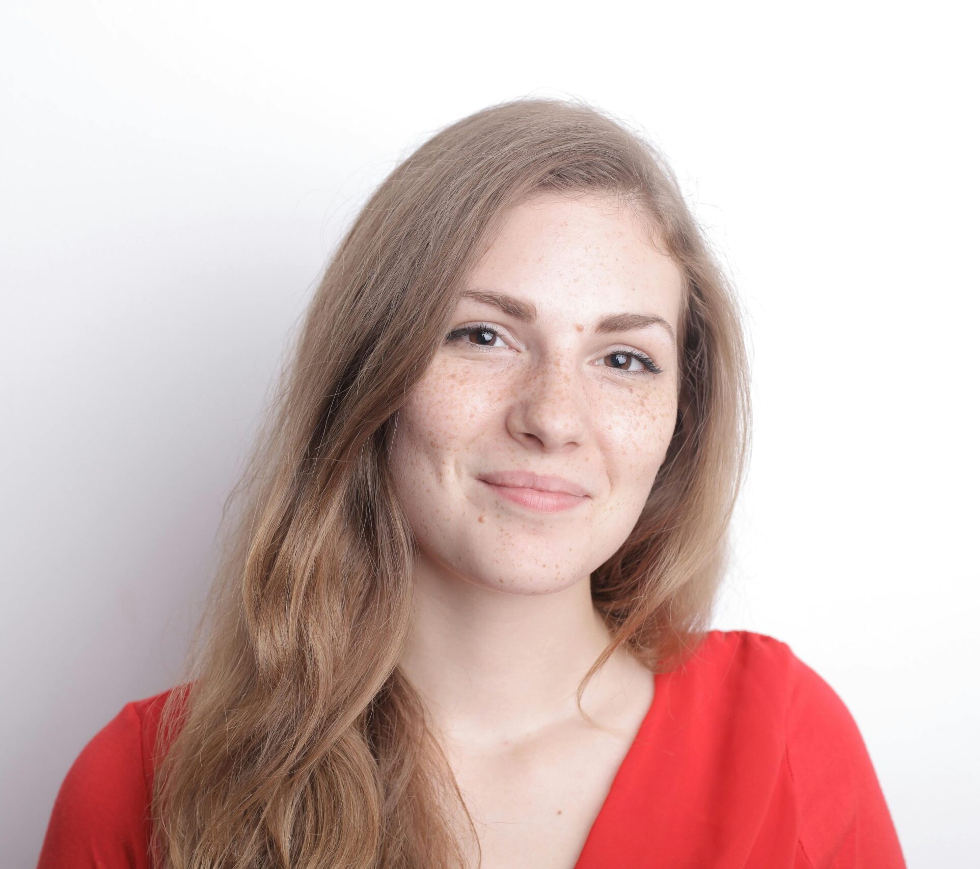 Portrait of a woman with freckles, smiling in a red blouse against a white background.