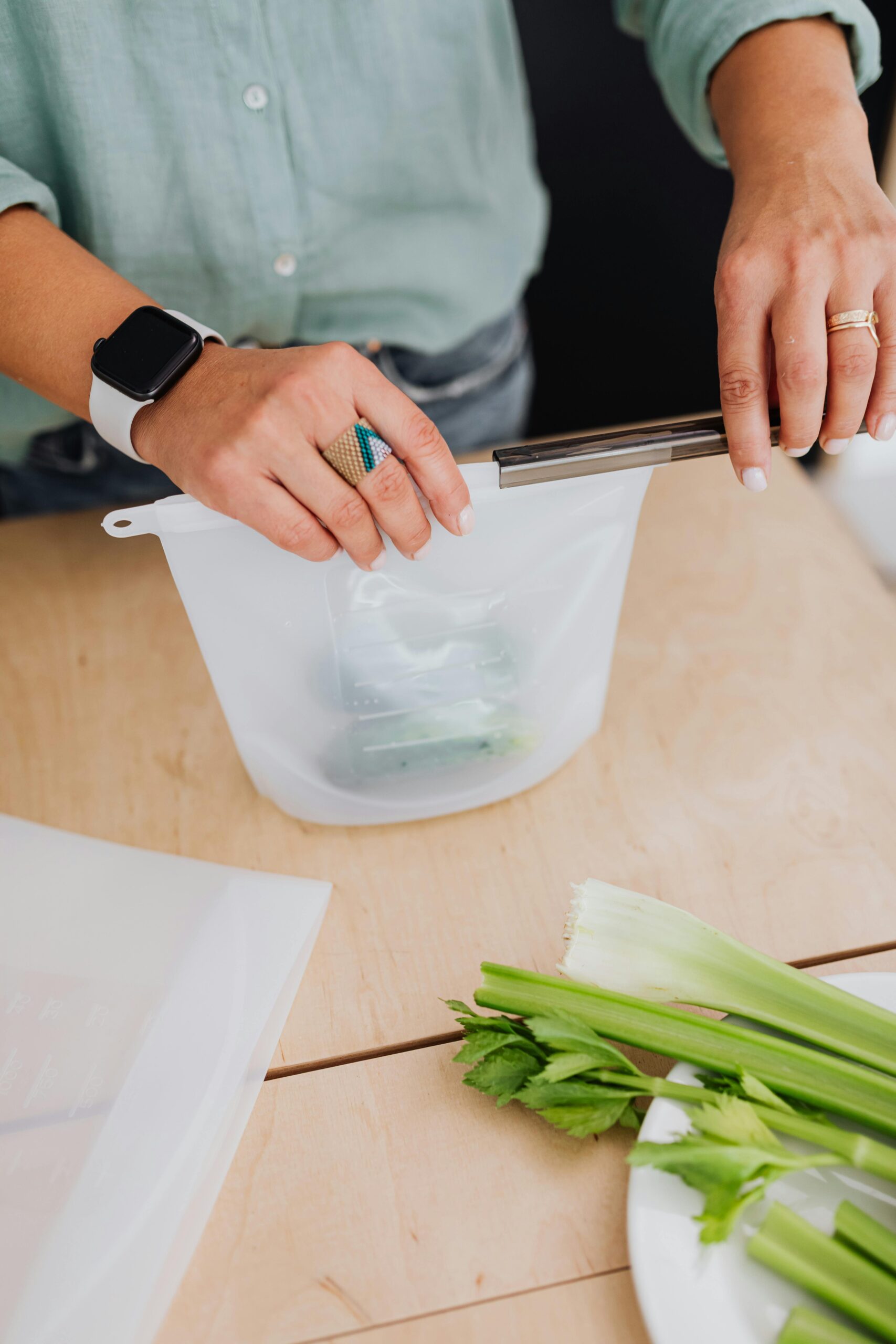 pexels photo 5237892 5237892 Hands sealing a reusable silicone bag on a kitchen table with fresh celery.