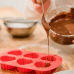 About Crop anonymous African American female adding sweet delicious melted chocolate in red heart shaped silicone baking dish