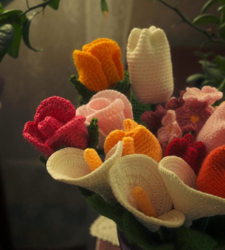About A vibrant bouquet of crocheted flowers in various colors, arranged in a vase.